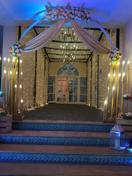 A rustic and romantic entrance design. We combined a fairy light tunnel with warm candle-like lights, wooden crates, and floral arrangements to create a charming welcome for the guests.