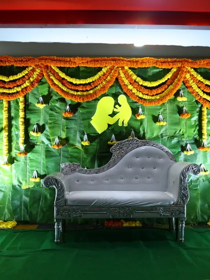 This is a classic setup for a traditional function, featuring a silver chaise lounge against a backdrop made of fresh banana leaves and marigold garlands.