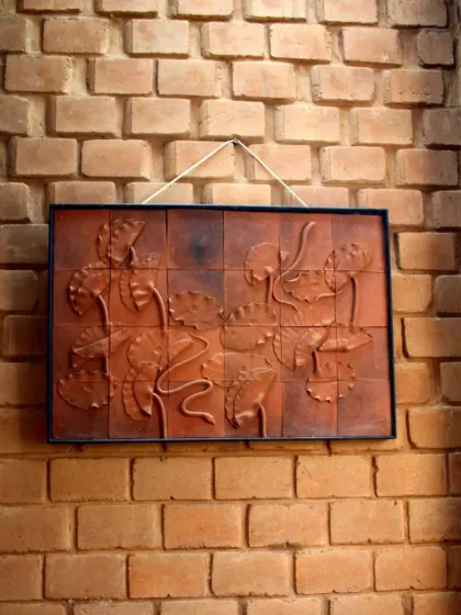 A framed terracotta tile mural depicting lotus flowers, hung against a textured brick wall. This piece highlights how we collaborate with artists to create custom works that complement the building's material palette.