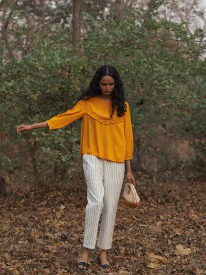 A full-body shot of a model walking through a forest setting. The vibrant yellow top stands out against the earthy tones of the fallen leaves, creating a beautiful and natural colour palette.