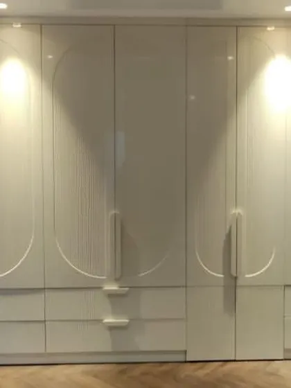 We designed this expansive floor-to-ceiling wardrobe to be a statement piece. It features a flawless high-gloss PU finish with custom CNC-milled circular patterns and integrated handles, creating a seamless and luxurious facade.