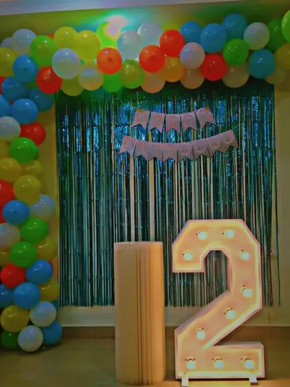 Bright and colorful for a 2nd birthday party. This setup includes a large light-up number "2", a vibrant multi-color balloon arch, and a teal shimmer curtain, creating a playful and cheerful atmosphere for a toddler's celebration.