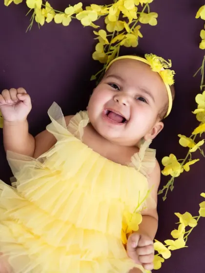 A burst of sunshine! A joyful shot of a baby girl in a bright yellow outfit against a matching floral backdrop.
