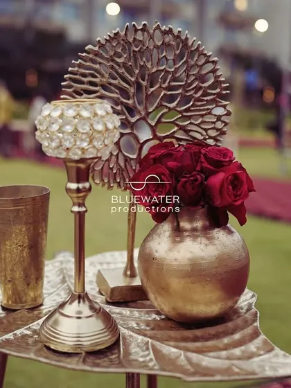 A small, elegant centerpiece featuring red roses in a brass vase, set on a leaf-shaped tray.