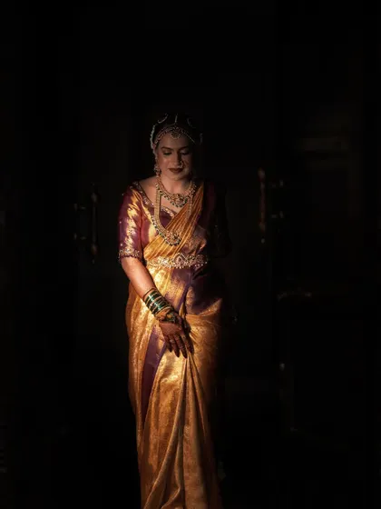 A dramatic portrait using a single light source. The bride, in a stunning golden saree, emerges from the darkness, creating a powerful and regal image.