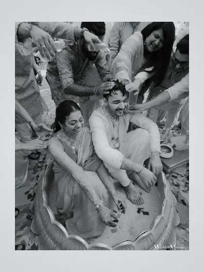 A black and white photo of friends and family showering the couple with blessings and turmeric during their Haldi. The monochrome effect adds a timeless and emotional quality to the moment.