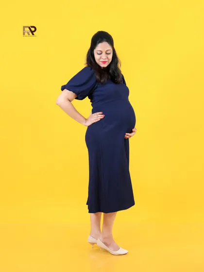 A simple and beautiful solo portrait. The mom-to-be cradles her bump, her navy blue dress standing out against the bright yellow backdrop.