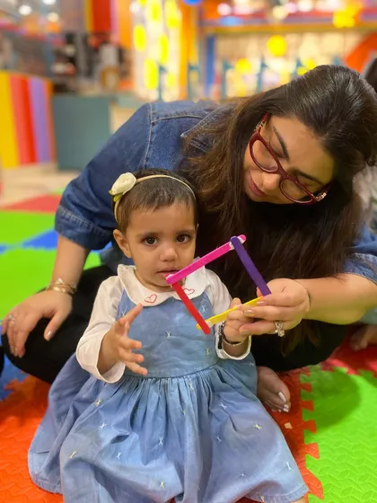 A mother helps her daughter hold up a colorful shape, celebrating their small but significant creative achievement.