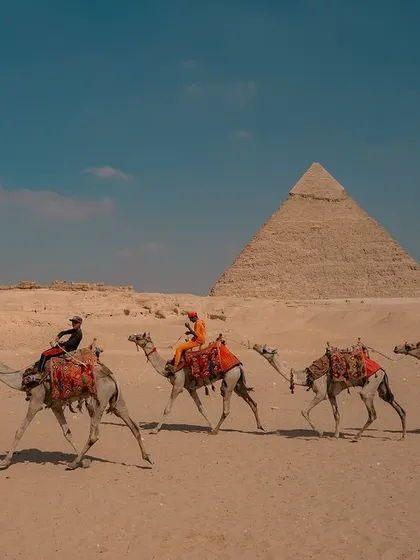 A caravan of camels carries tourists across the desert with the Great Pyramids of Giza in the background. A timeless scene of travel and exploration.
