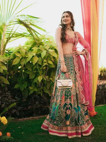 A full-length portrait of the bride, showcasing her elegant Sangeet attire against a lush green background.