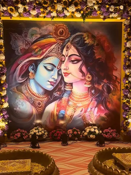 A closer view of the divine Radha Krishna backdrop. The rich colors of the painting are complemented by the vibrant floral frame, creating a perfect setting for a sacred Haldi function.