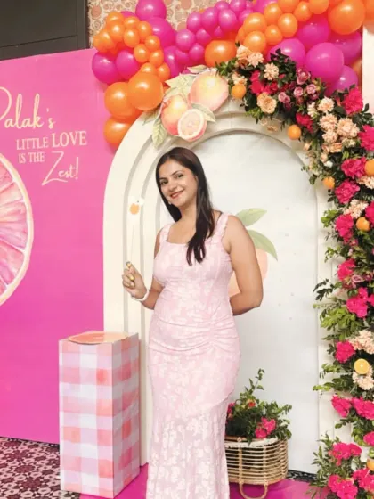The happy mom-to-be at her vibrant citrus-themed baby shower. The decor features a bright pink and orange color scheme with a floral and fruit arch.