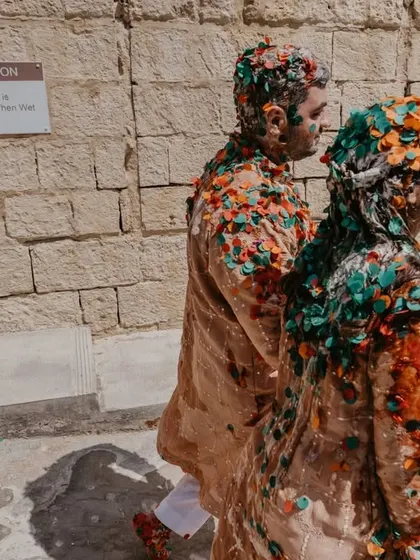 The couple, covered in colorful flower petals, walking through the historic stone corridors of their Malta venue after the haldi.