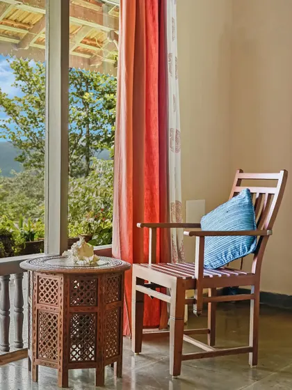 A quiet corner on the veranda with a view of the lush green valley. The carved wooden table and colorful curtains create a perfect spot for a morning cup of tea.