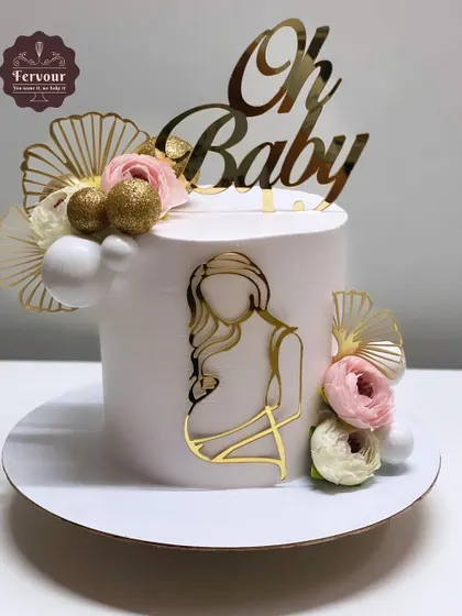 A beautiful "Oh Baby" cake for a mom-to-be. The clean white design is accented with gold acrylic toppers, delicate fans, and soft pink flowers, creating a chic and modern baby shower cake.