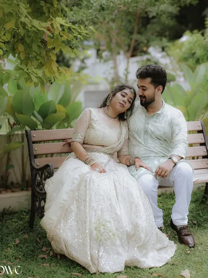 A romantic portrait of a couple on a bench, with the bride-to-be resting her head on her partner's shoulder.