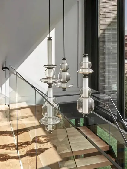 A trio of Luna Kaleido pendants cascades down a modern staircase, creating a dramatic vertical feature and casting beautiful shadows on the surrounding walls.