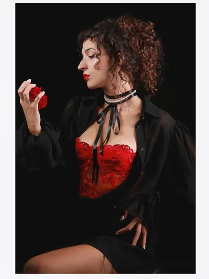A vintage-inspired portrait with a modern twist. The combination of a red lace corset, a black sheer shirt, and dramatic lighting creates a look of old Hollywood glamour.