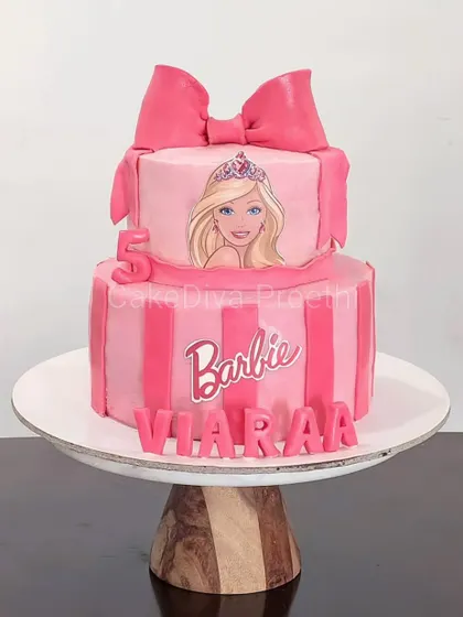 Hi Barbie. I finally got to make a cake for the Barbie trend. This two-tier pink cake features stripes, an edible image of Barbie, and a large, handcrafted fondant bow on top.