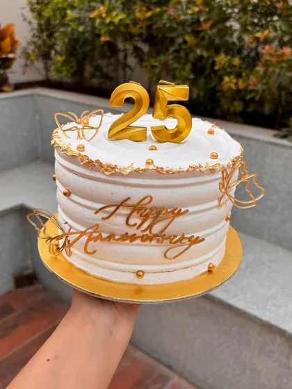 Celebrating a 25th anniversary with this elegant white and gold cake. It features a "25" candle topper, gold butterfly accents, and a "Happy Anniversary" sign.