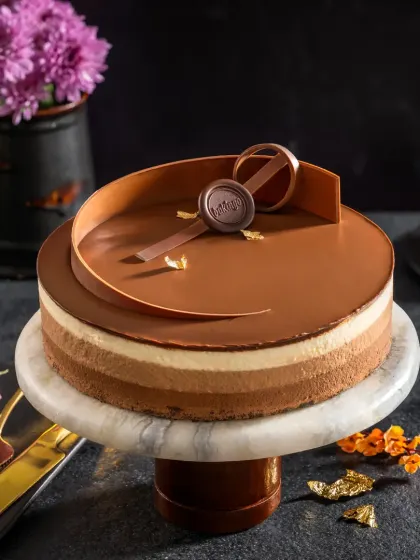 An elegant shot of a triple-layered chocolate mousse cake for Bakingo. I used a dark, minimalist setup to emphasize the cake's glossy finish, clean layers, and the delicate chocolate swirl decoration, making it look absolutely luxurious.
