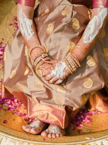 An artistic detail shot of the bride's hands and feet, covered in paste and surrounded by petals in a large brass thali. This frame captures the textures and traditions of the Haldi ceremony.