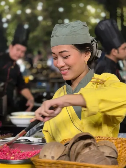 Our chefs' passion for their craft is evident in their smiles. Here, a chef joyfully prepares a colourful rice dish at a live station, engaging with guests and sharing her love for food.