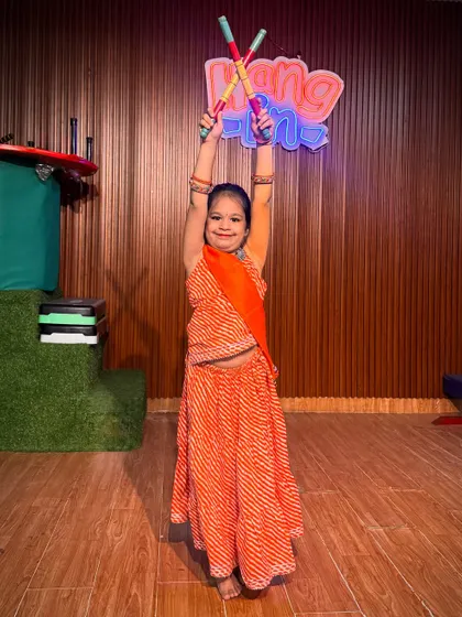 Dressed in a vibrant orange bandhani lehenga, this student holds her dandiya sticks high. This photo highlights the colorful and festive atmosphere of our Navratri dance workshops.