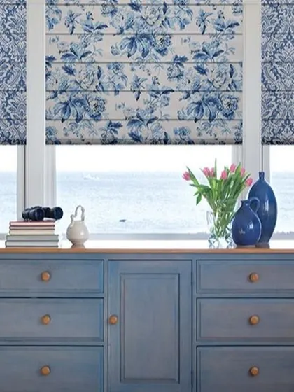 These Roman blinds feature a classic blue and white floral damask pattern. They bring a touch of timeless elegance to the room, perfectly matching the coastal-inspired decor.