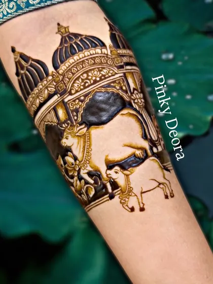 A close-up of the Shreenathji temple and cow design, set against a beautiful natural background. The dark henna stain makes the intricate details stand out.