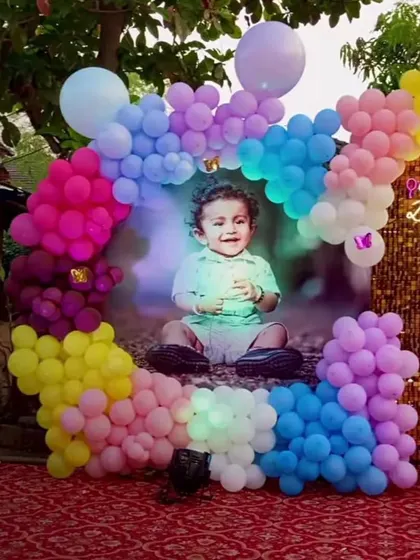A colorful outdoor setup for a first birthday party. The circular balloon frame with a large photo of the birthday boy makes for a wonderful and personal photo corner.
