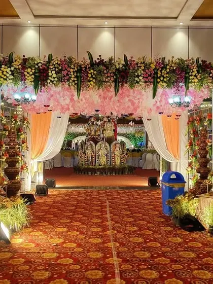 A grand entrance for a traditional wedding, flanked by large, golden statues of Lord Ganesha and other deities. The floral arch and rich carpeting create a royal welcome for guests.