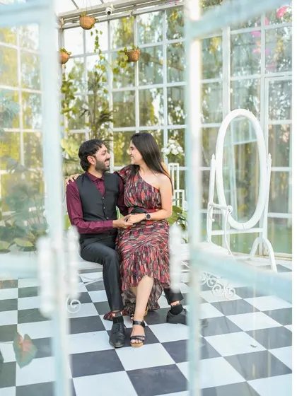 A lovely portrait of the couple seated inside the glasshouse, framed by the window panes for an artistic effect.