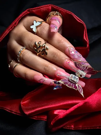 The nails against a rich red satin background, making the delicate pink and purple tones pop.