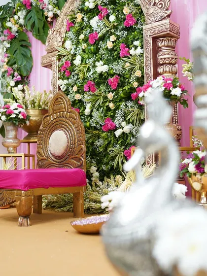 A beautiful setup for an intimate celebration, featuring a traditional gold chair against a stunning floral arch. The combination of pink and white flowers with gold accents creates a regal and elegant look.