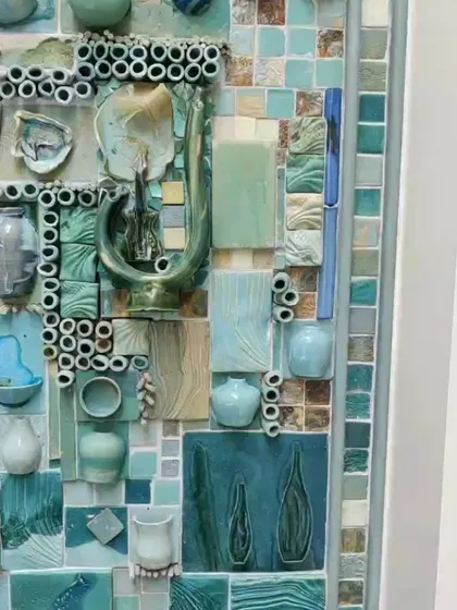 A close-up of the ceramic mural, where you can see the individual, three-dimensional pieces. There are small pots, fish, and abstract shapes, all glazed in beautiful shades of turquoise and green.