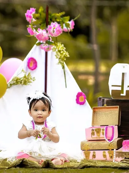 A candid moment from an outdoor first birthday shoot, where the birthday girl is taking a break from her cake to play.