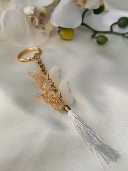 This delicate butterfly keychain is made with white and gold-flaked resin and finished with a white tassel. It's a sweet and whimsical accessory.