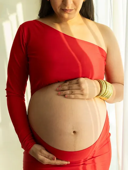 A sun-kissed portrait. The natural light streaming from the window beautifully highlights the texture of her skin and the curve of her belly.