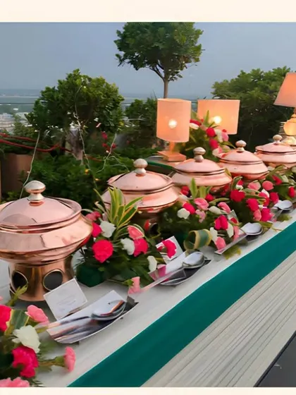 A daytime buffet setup on a rooftop, featuring our classic copper chafing dishes. The table is beautifully decorated with pink and white flowers, creating a fresh and vibrant look for a pre-wedding celebration.