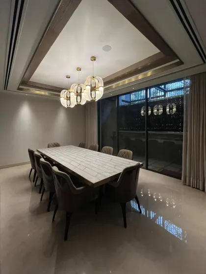 This dining room blends modern forms with Art Deco elegance. A large, minimalist dining table is surrounded by plush, comfortable chairs, while a series of geometric, Art Deco inspired chandeliers with gold accents provide a dramatic focal point.