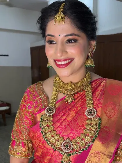 A radiant smile from Dr. Harshitha on her Muhurtham day. I used a classic red lip and warm, shimmery eyeshadow to complement her pink Kanjivaram saree and antique gold jewelry.