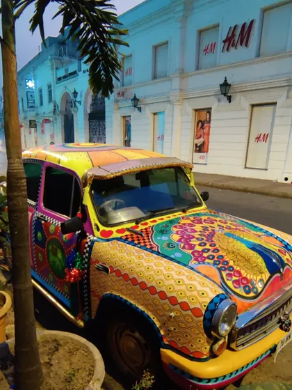 The painted Ambassador parked on a city street, looking like a vibrant piece of pop art against the urban backdrop.
