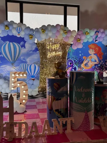 I specialize in creating combined themes for twins' birthdays, ensuring both children feel celebrated. This setup seamlessly blends a hot air balloon theme and a mermaid theme with two distinct backdrops united by a central shimmer wall.