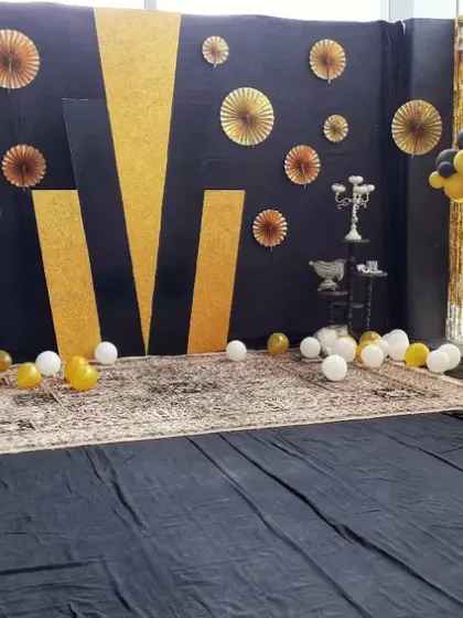 A modern and glamorous party backdrop with a black and gold theme. This setup includes a geometric background, gold tinsel curtains, and decorative trees made from balloons.