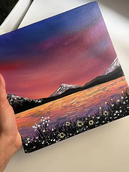 A finished acrylic painting of a rainbow sky over a lake and mountains. The vibrant colors make this landscape feel so magical.