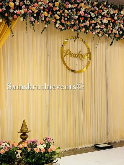 A simple yet elegant engagement backdrop with golden drapes and a personalized name sign. The floral arrangements in shades of pink and peach add a soft, romantic touch.