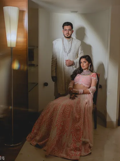 A formal and regal portrait of the couple. The bride is seated while the groom stands behind her, creating a classic composition that exudes elegance and sophistication.