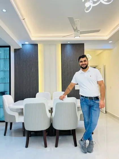 Standing in a completed dining area. The space features a sleek white dining table with comfortable upholstered chairs, set against a backdrop of a dark fluted wall panel that adds texture and contrast.