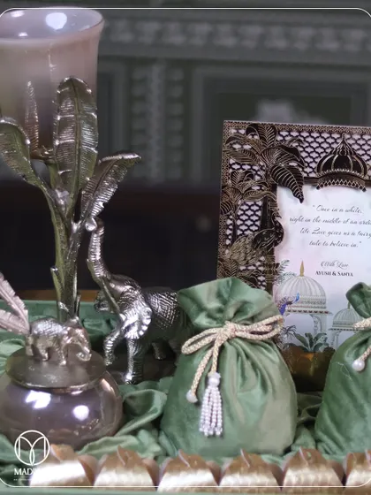 A regal welcome for your guests. This wedding hamper features silver elephant figurines, a detailed brass frame for the invite, and green velvet potlis, creating a luxurious and traditional gifting experience.